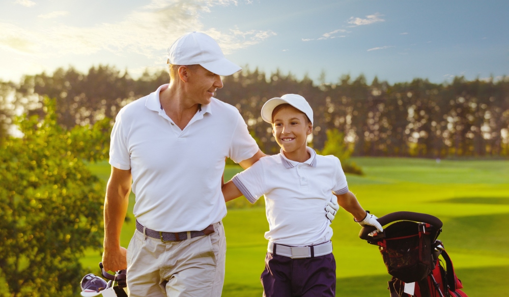 Happy man with his son golfers walking on perfect golf course at summer evening