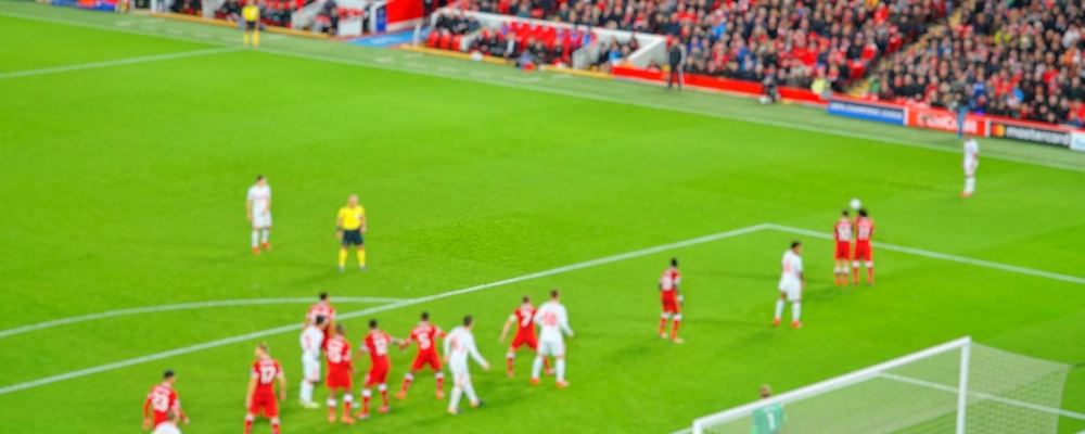 Blurred background of football players playing and soccer fans in match day on beautiful green field with sport light at the stadium. Sports,Athlete,People Concept.Mercy side,Anfield,Liverpool. ; Shutterstock ID 1082801411