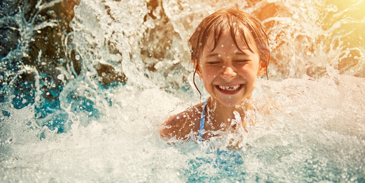 Little girl playing in waterfall in waterpark swimming pool