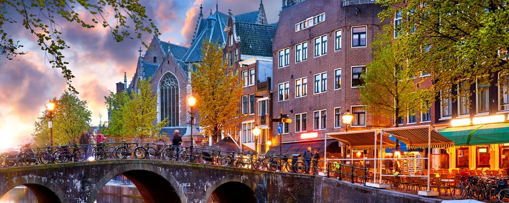 Red-light district in Amsterdam city picturesque landscape panorama evening town with pink sunset sky. Bridge over canal river Amstel.