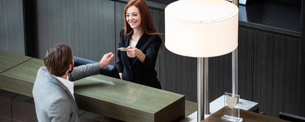 Smiling female receptionist giving credit card to businessman while standing at hotel reception