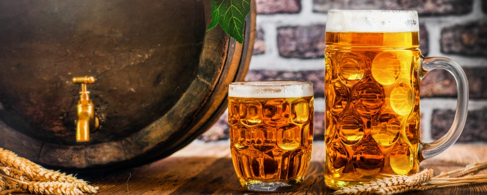 Beer glasses and beer barrel with wheat on wooden table