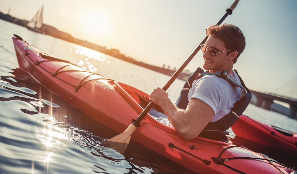 Handsome sporty man is kayaking on sunset. Canoeing alone.