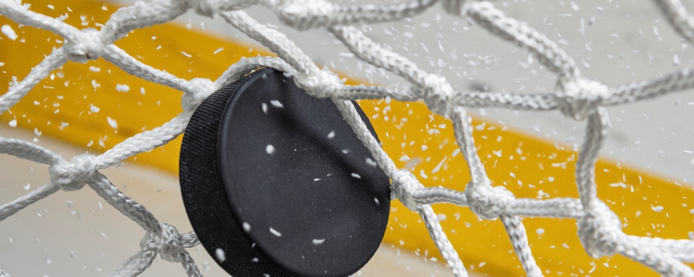 A close-up view of an Ice Hockey puck hitting the back of the goal net as shavings fly by, viewed from the front. Scoring a goal in ice hockey.