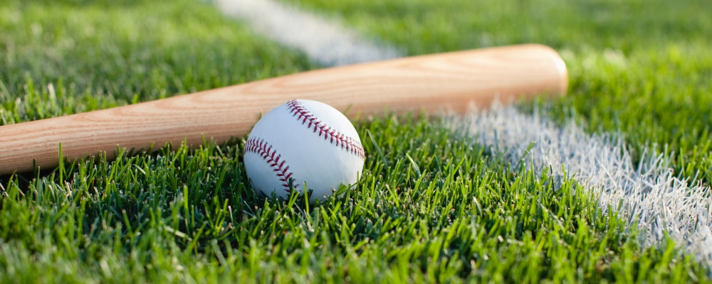 A selective focus view of a baseball bat and ball on the grass near a field stripe