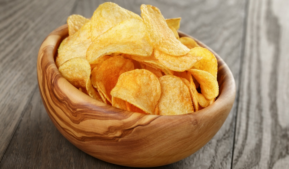organic potato chips in bowl on wood table, close up