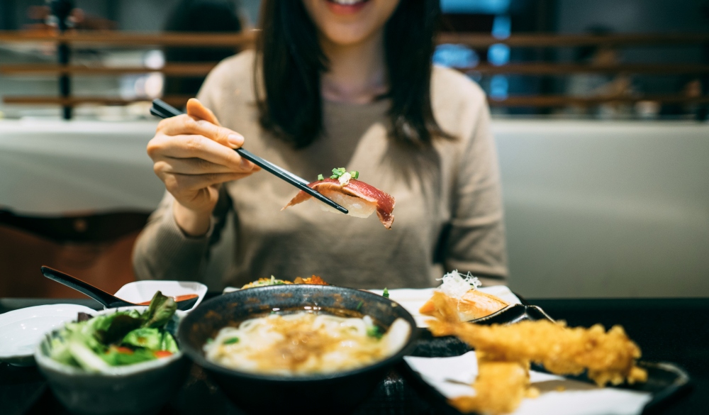 Joyful young woman enjoying sushi, seafood tempura, soup udon, salad and green tea in a Japanese restaurant