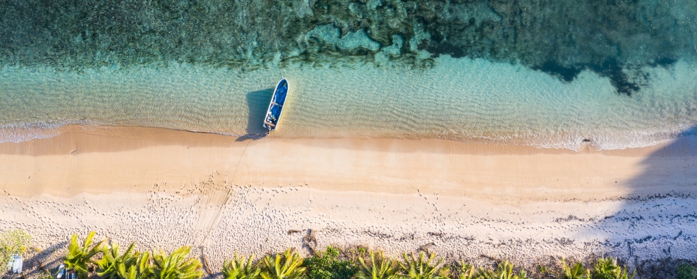 Top down view of an idyllic island with a boat, palm trees and coral reef in Fiji in the south Pacific ocean