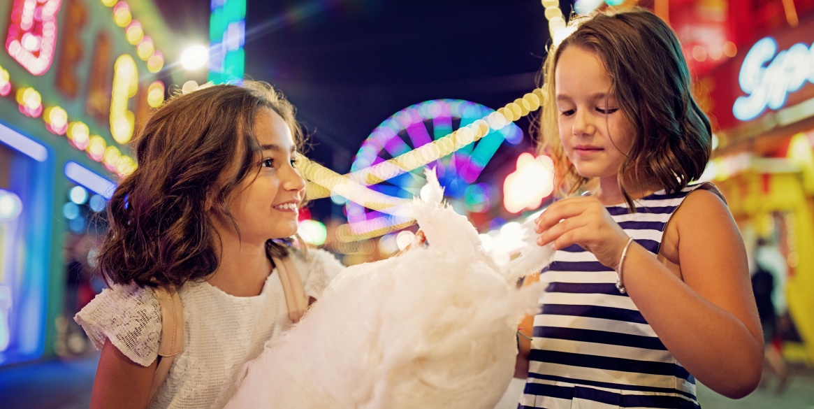 little girls are eating cotton candy at the fun fair and making fun