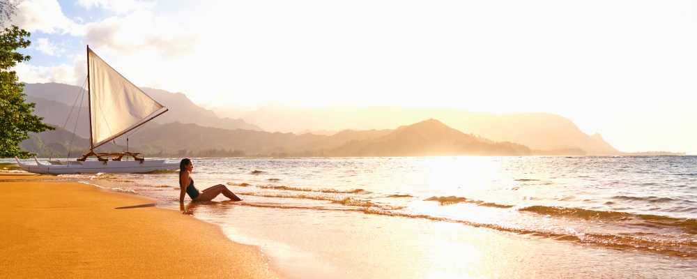 kobieta siedząca na plaży w pobliżu żaglówki