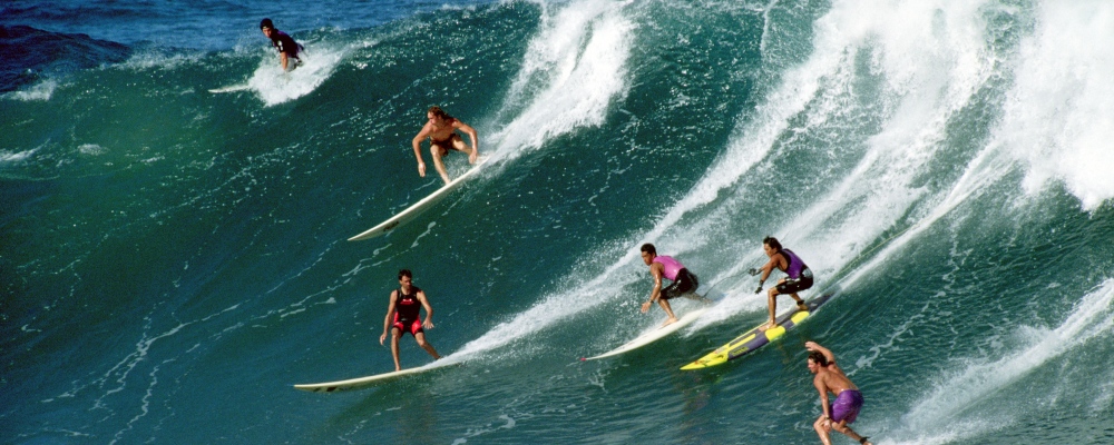 Surfers die in een golf vallen in Waimea Bay