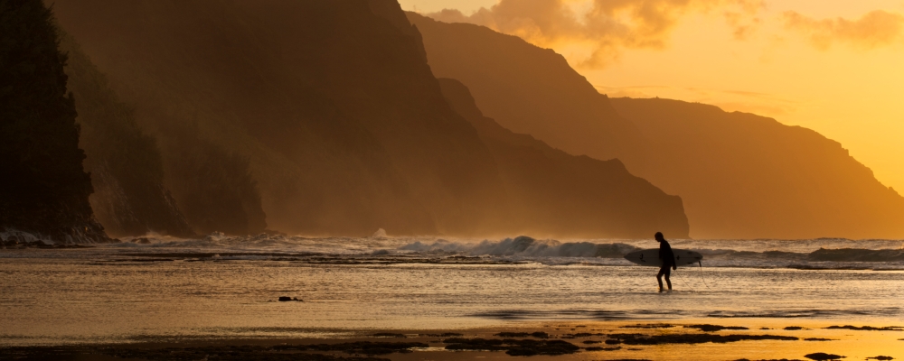 Surfista en la playa y la Costa Na Pali vista desde Ke'e beach, Ha'ena