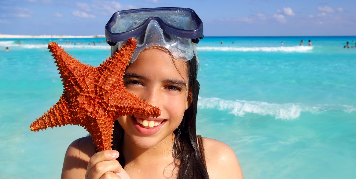 Latin tourist girl holding a starfish at a tropical beach, Riviera Maya kid friendly