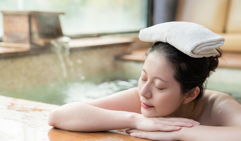 japanese girl lying down on poolside sleep and put a towel on her head while water flows on the background.