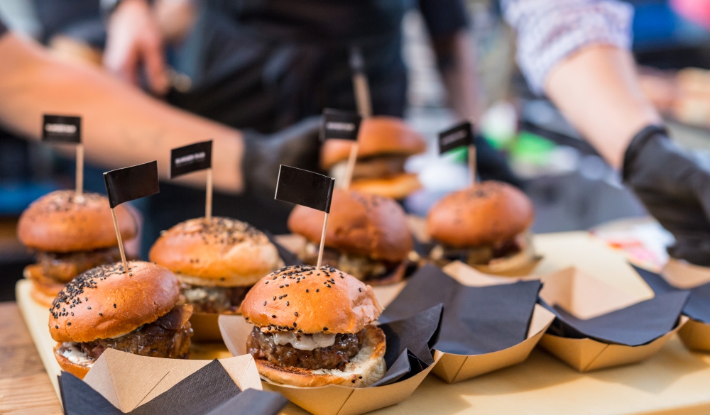 Chef making beef burgers outdoor on open kitchen international food festival event. Street food ready to serve on a food stall.