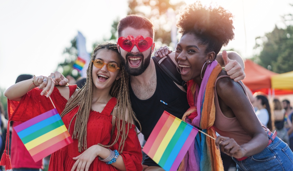 Young beautiful people celebrating the pride event, hugging, waving rainbow pride flags and having fun