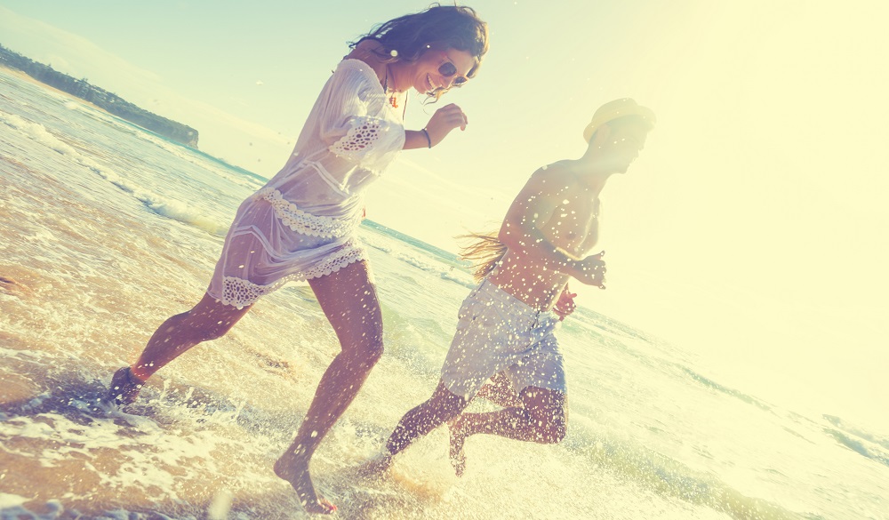 Smiling young people running on the beach in the sun