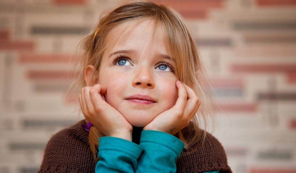 Little dreamy girl, resting face on her hands, lying on her belly in museum.