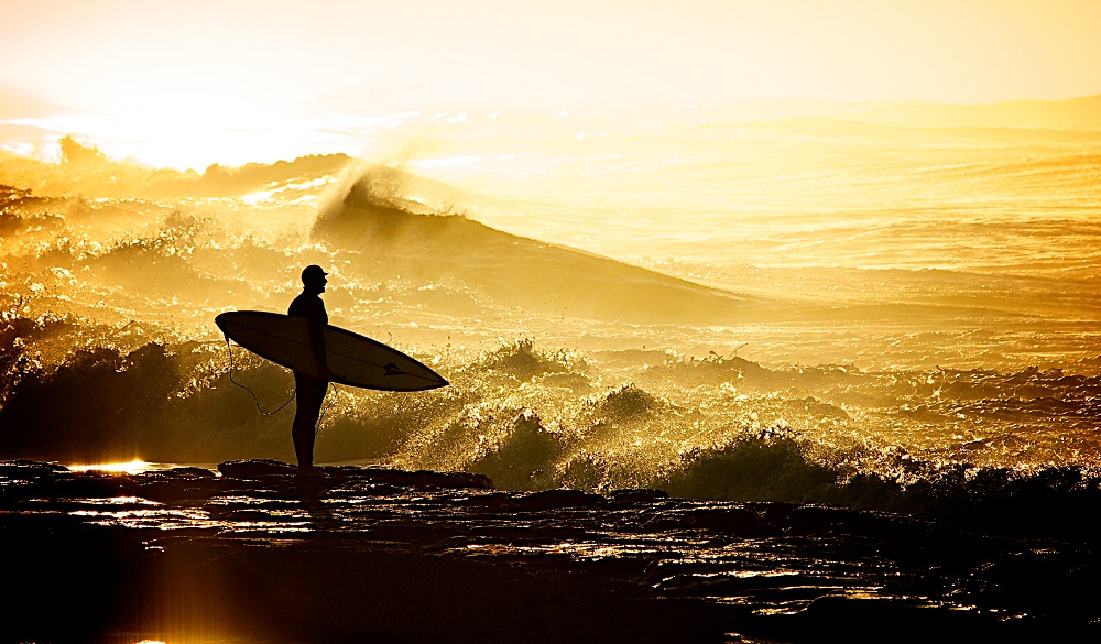 Silhouette of surfer holding surfboard on rocks in Merewether beach.