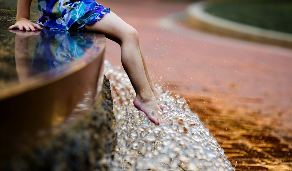 Bare kids' feet dangling in the water feature /public fountain.