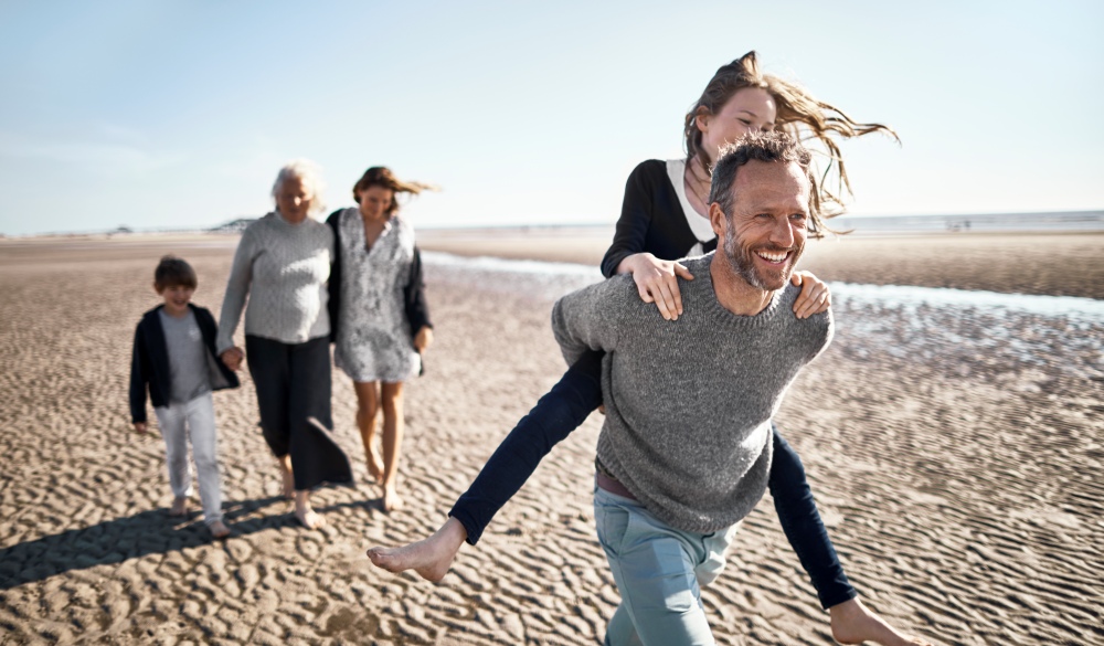 Happy father carrying daughter piggyback on the beach, spring break destinations