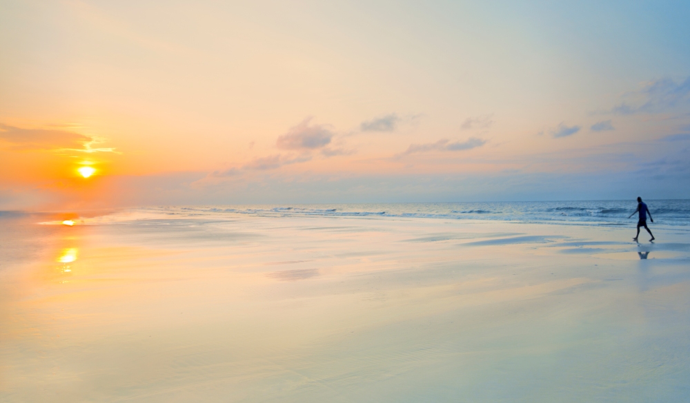 Person walking on the beach at sunrise, spring break destinations