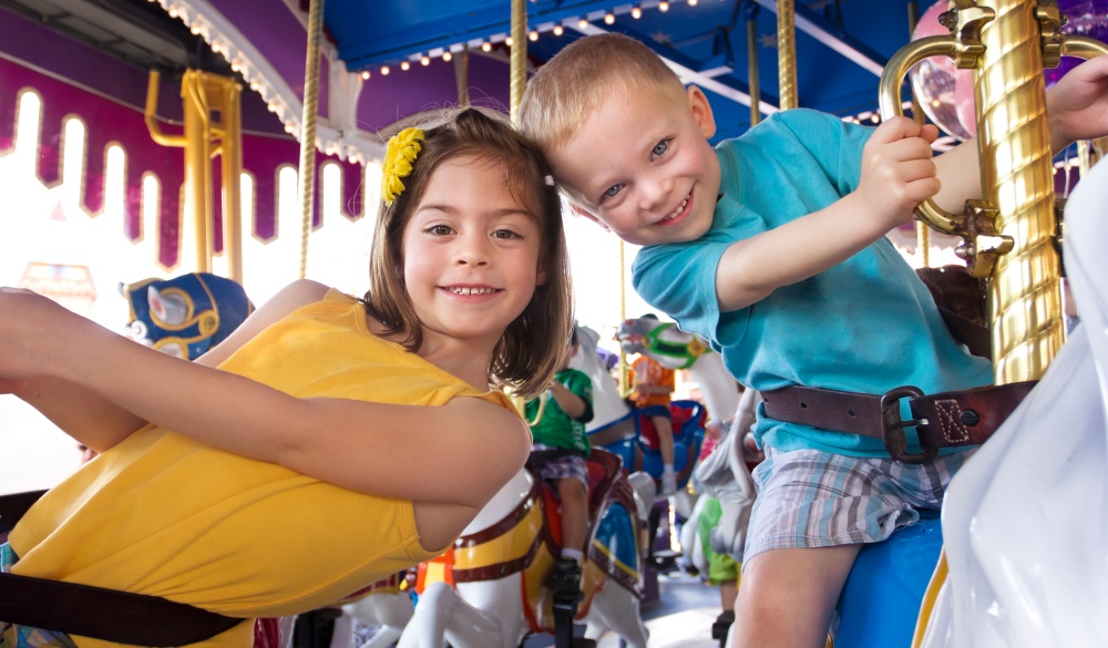 Two cute kids having fun while riding a carousel at an amusement park or carnival