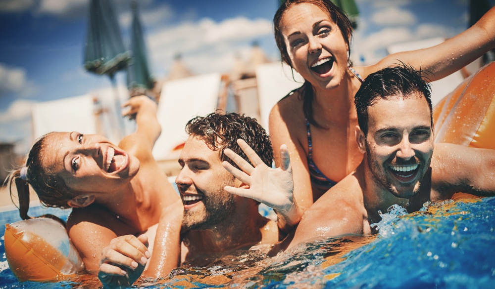 Closeup front view of group of young adults having fun in a swimming pool on a hot summer day. There are two girls and two guys trying to get on a pool raft. Toned image.