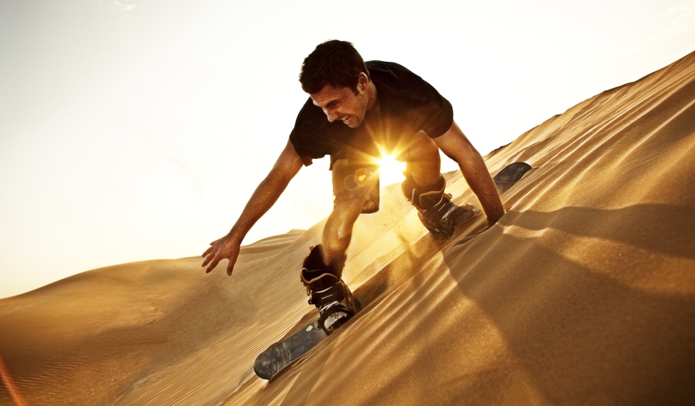 man sand boarding on the sand dune called Big Red in the desert near Dubai