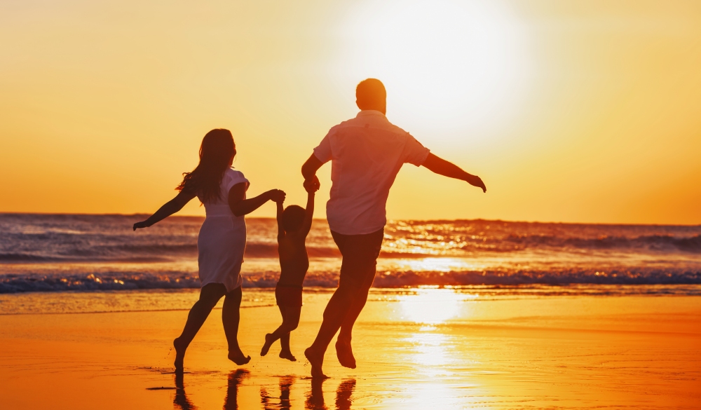 Happy family - father, mother, baby son hold hands and run with fun along edge of sunset sea on black sand beach. Active parents and people outdoor activity on tropical summer vacations with children.