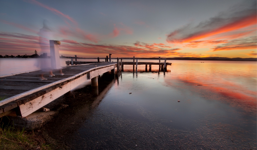 White ghost-like figure walking down Squid's Ink Jetty, Lake Macquarie, NSW at sunset.