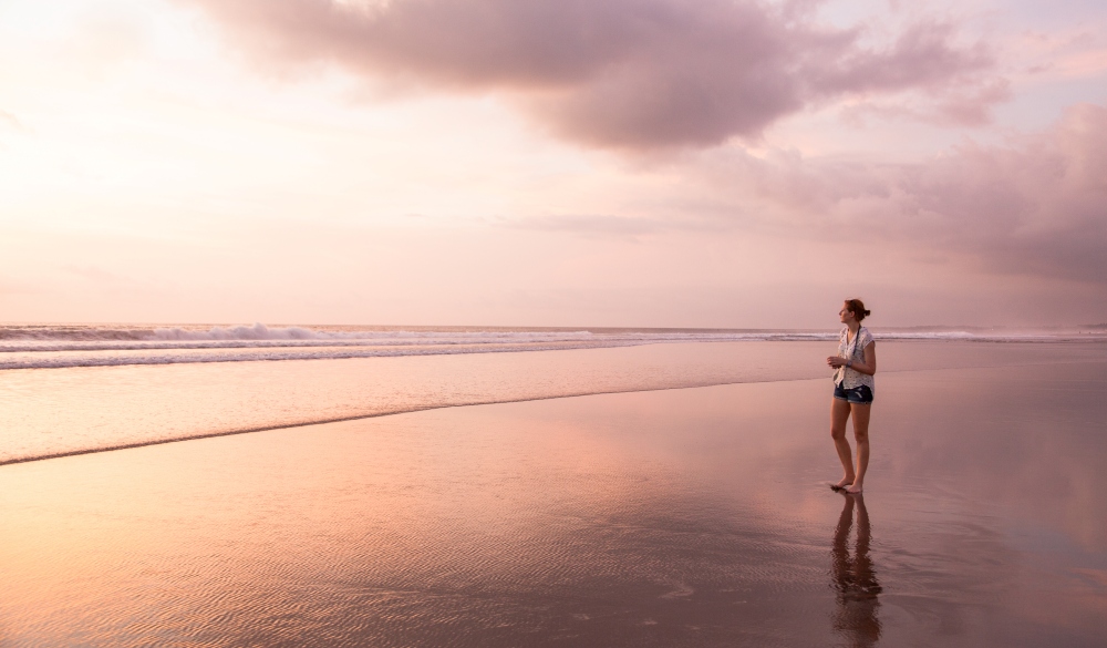 The Beach between Legian and Seminyak just before sunset. One attractive young woman is walking on the sandy beach in the shallow waters. Seminyak beach, Kuta, Bali, Indonesia.