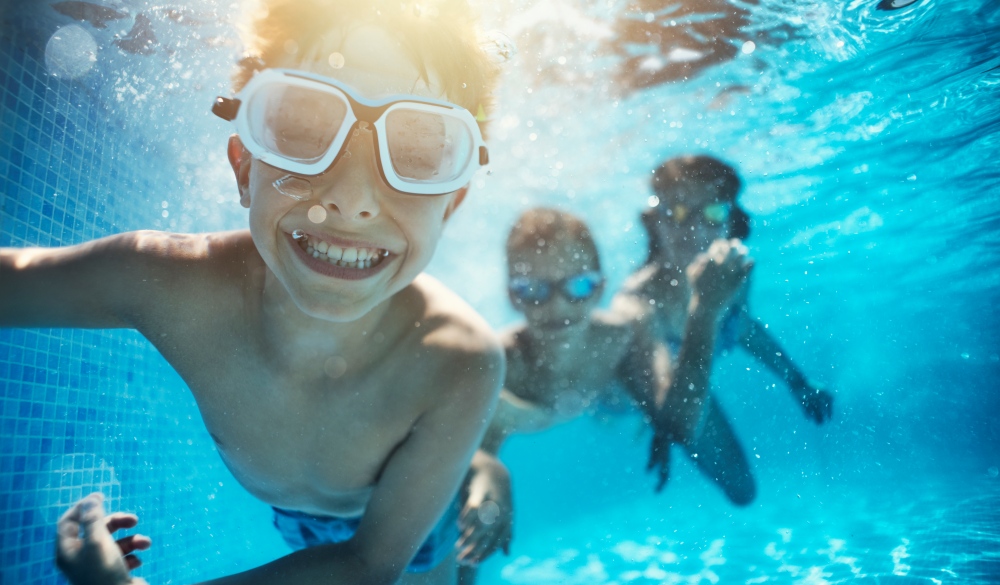 Happy kids having underwater party in the swimming pool. The boy is grinning at the camera. 
Shot with Nikon D850.