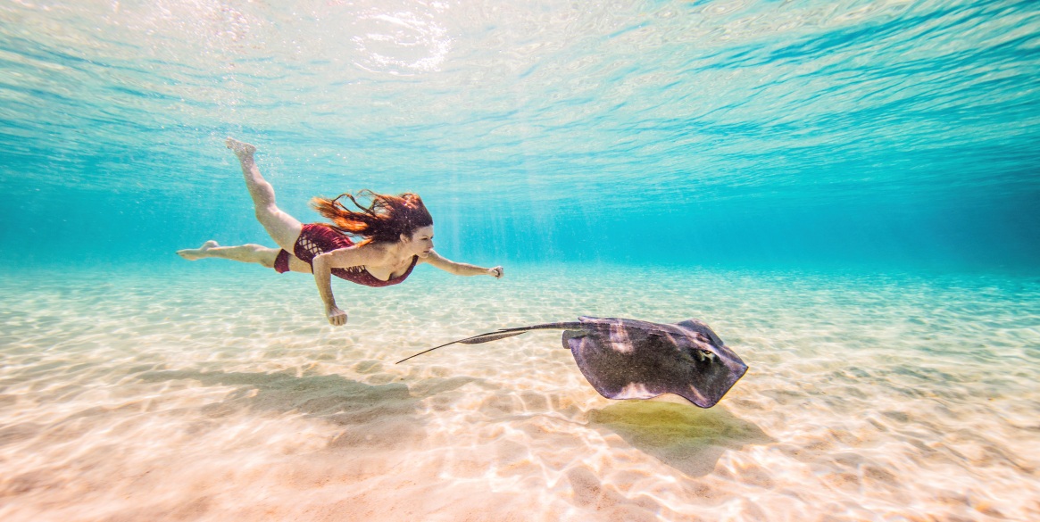 Female free diver swimming with stingray on seabed