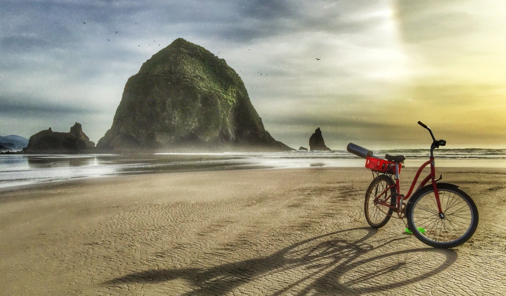 During sunset: a view of Haystack Rock with the shadow from a red bicycle on the shoreline of Cannon Beach, Oregon.