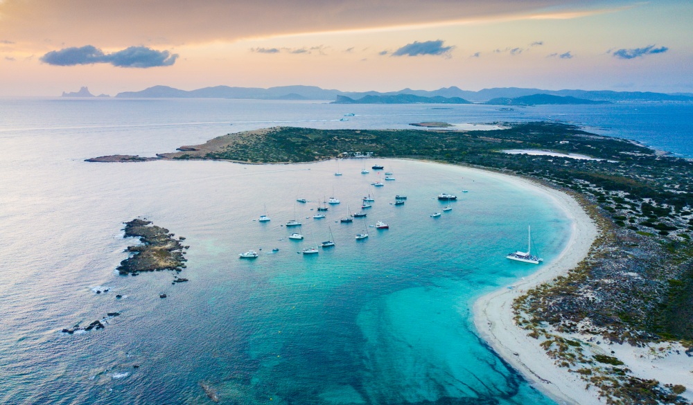 Aerial landscape view of Espalmador and Ibiza during sunset with sailboats anchored.