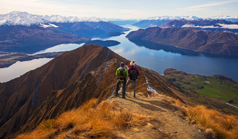 Two young women climb up and look out over the viewpoint at the top of Mt. Roy in New Zealand