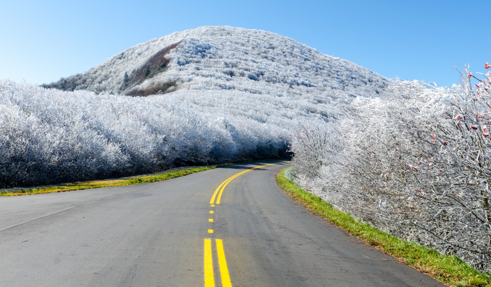 Landscape of frozen mountains along the Blue Ridge Parkway at Graybeard Mountain. The road winds into the mountains with the yellow lines visible in the centre of the road. The Blue Ridge Parkway is a popular road trip especially in the fall season.