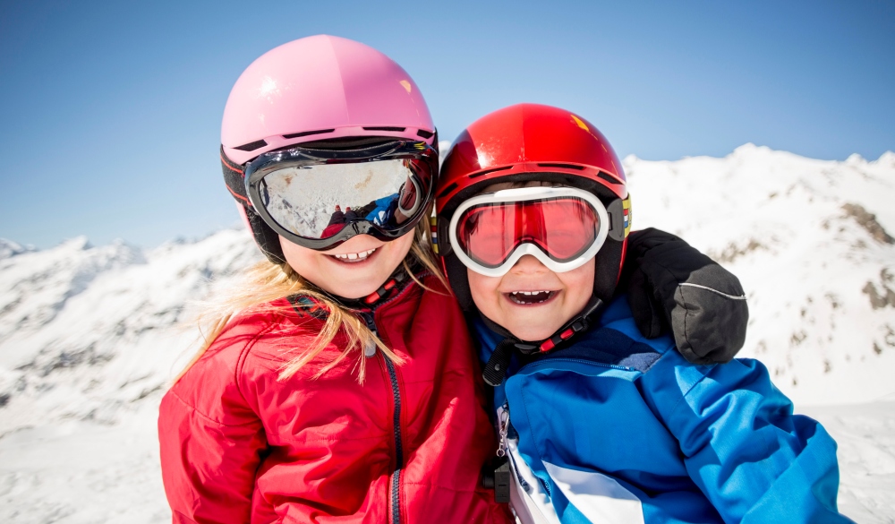 Cheerful siblings in ski-wear standing against snowcapped mountain