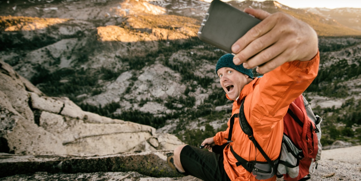 A man takes a selfie on a cliff in the backcountry