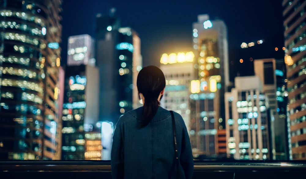Rear view of woman standing by the roof terrace overlooking spectacular city skyline at dusk