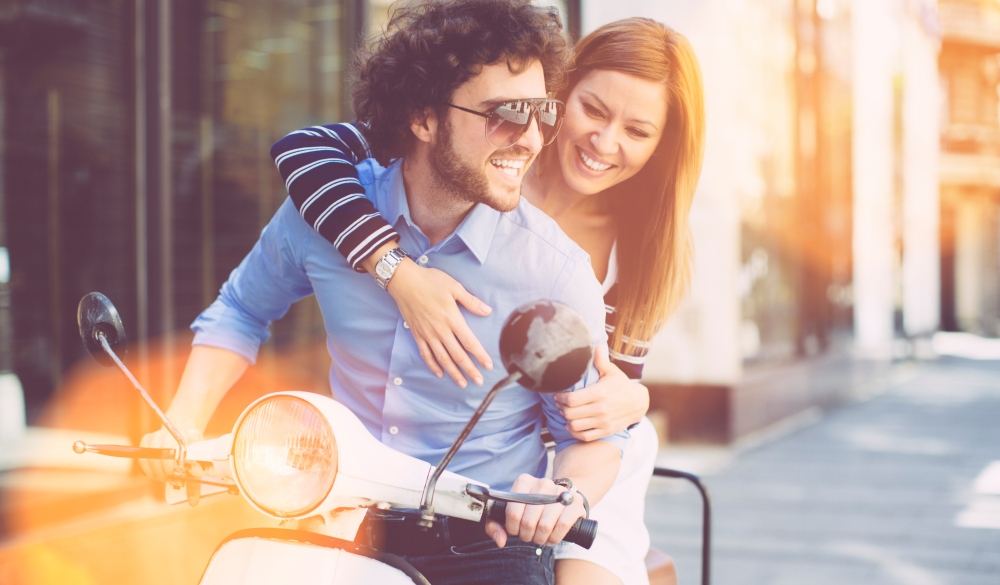 Cheerful Young Couple Riding on a motorbike and having fun together. Woman sitting on back and embracing her man.