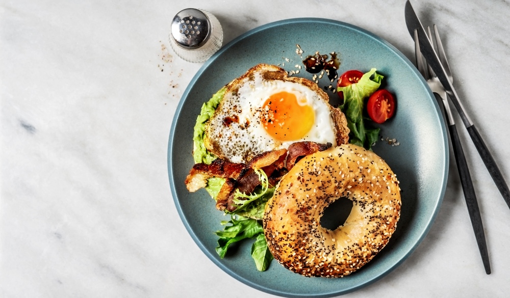 Bagel sandwich with avocado, fried egg and side salad on white background