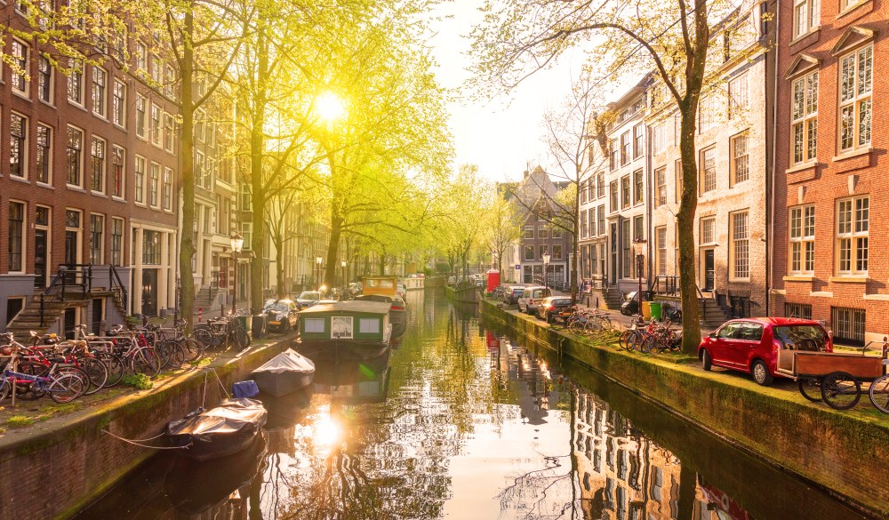 This is a picture taken on the Raamgracht early in the morning. This canal is around Nieuwemarkt a very touristic place in the center of Amsterdam. Early in the morning, before the city wakes up it is nice and not busy. Without any boats passing by, the waters are calm and make excellent reflection of the rising sun.