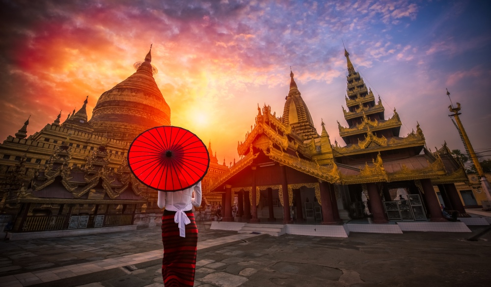 Burmese woman holding traditional red umbrella and looks at Golden Shwezigon pagoda in Bagan, Myanmar