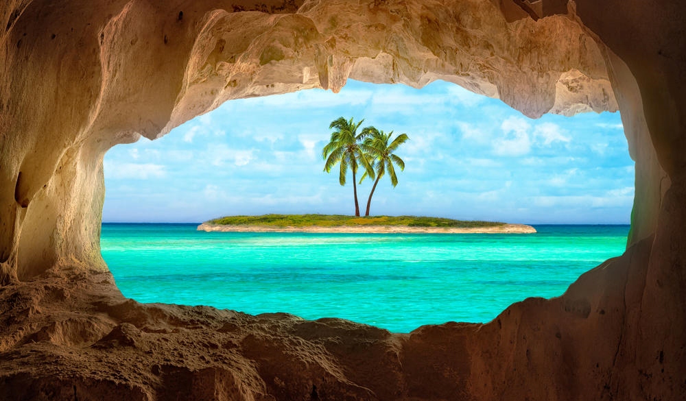 An old Indian cave located on a remoteTurks and Caicos Island. Beautiful Caribbean sea glowing and warm sunlight bathing some remote palm trees on a deserted island.