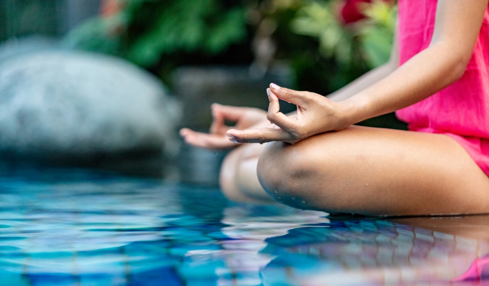Woman practicing yoga on swimming pool edge, focus on closer hand