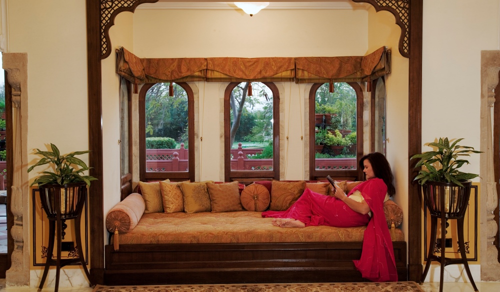 Tourist sitting on couch by bay window of a historical suit in Taj Rambagh Palace Hotel in Jaipur, part of the Taj Hotel Group. India. (MR)