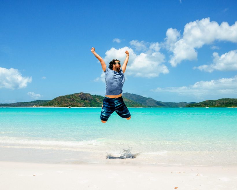 Australia, Queensland, Whitsunday Island, carefree man jumping at Whitehaven Beach