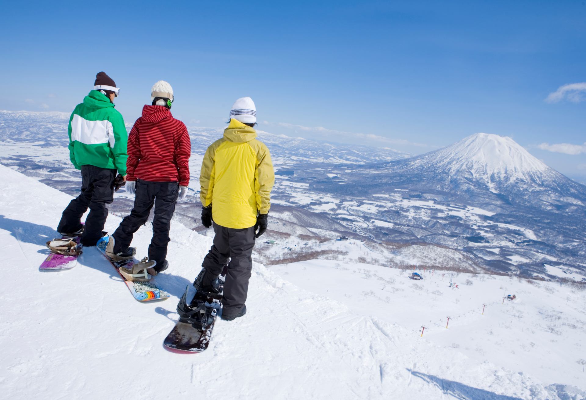 Three snowboarders on edge of slope, rear view